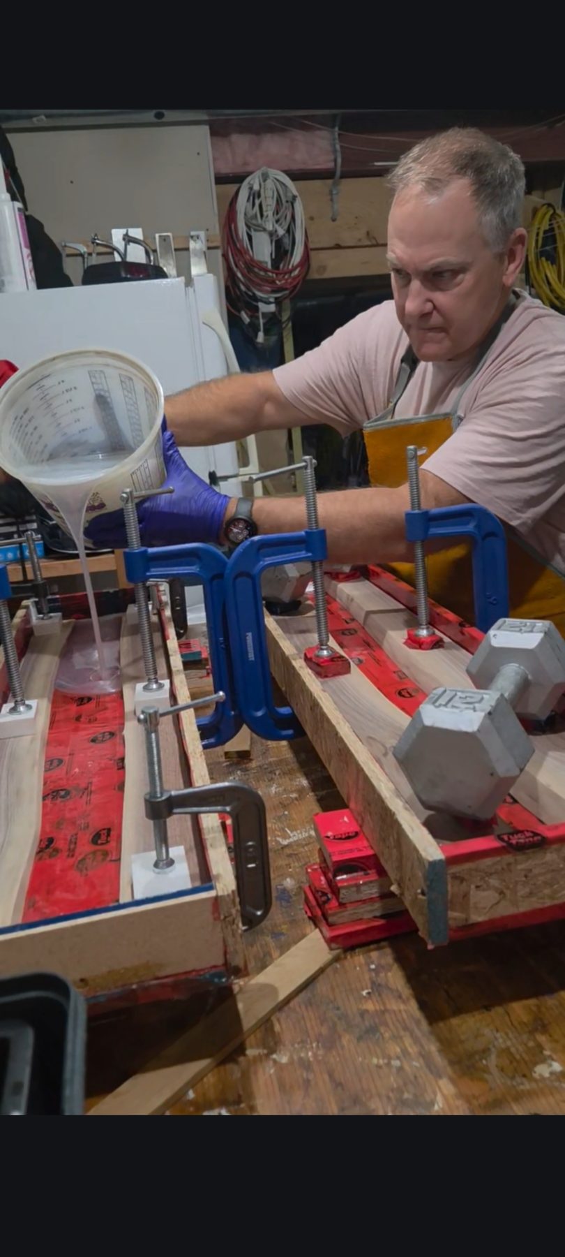 Pouring epoxy resin into a clamped live-edge slab in the workshop